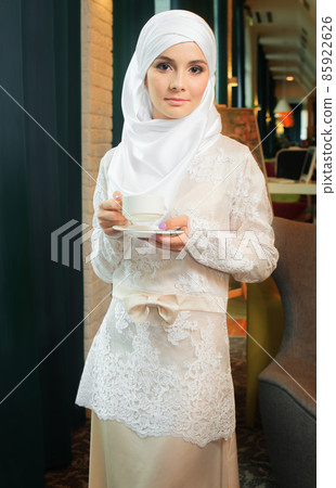 Muslim woman in a white wedding dress with a cup of tea in his hands Muslim woman in a white wedding dress with a cup of tea in his hands 85922626