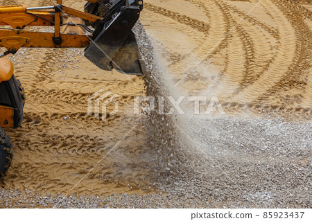 a bulldozer pours gravel from a bucket onto the compacted sand at a construction site a bulldozer pours gravel from a bucket onto the compacted sand at a construction site 85923437