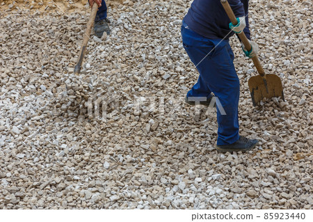 two construction wrokers shoveling white macadam during road construction process 85923440