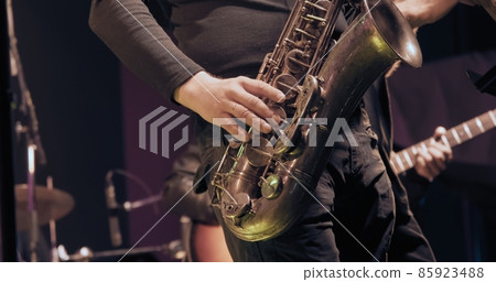 Man saxophonist at a concert plays the saxophone. Live musical performance and virtuosity of playing a brass musical instrument. It dark, colored spotlights are shining around 85923488