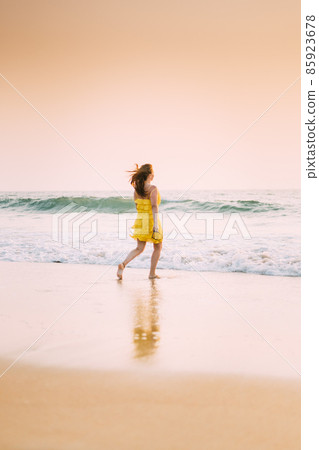 Goa, India. Young Caucasian Woman In Yellow Dress Enjoying Life And Running Towards Sea Waves 85923678