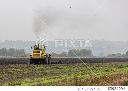 grim yellow tractor plows the field after harvest before winter at cloudy and foggy autumn morning 85924094