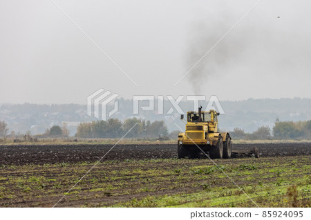 grim yellow tractor plows the field after harvest before winter at cloudy and foggy autumn morning 85924095