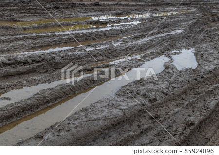 A broken rural country road after the rain. Puddles after rain on a dirt road. Clay, soil and puddles at cloudy day light after rain, autumn season. A broken rural country road after the rain. Puddles after rain on a dirt road. Clay, soil and puddles at cloudy day light after rain, autumn season. 85924096