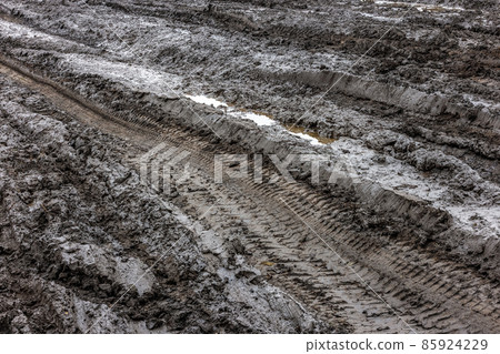 A broken rural country road after the rain. Puddles after rain on a dirt road. Clay, soil and puddles at cloudy day light after rain, autumn season. 85924229