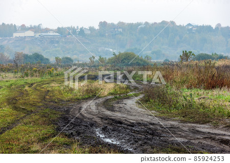 autumnal foggy morning rustic lansdcape with dirt road in the foreground and small buildings on hill in the background autumnal foggy morning rustic lansdcape with dirt road in the foreground and small buildings on hill in the background 85924253