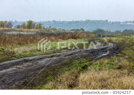 autumnal foggy morning rustic lansdcape with dirt road in the foreground and small buildings on hill in the background autumnal foggy morning rustic lansdcape with dirt road in the foreground and small buildings on hill in the background 85924257