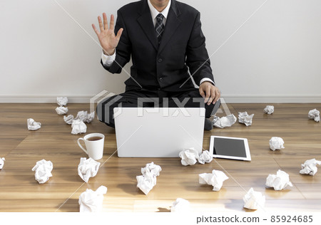A man in a suit sitting on the floor and making a video call on his laptop and a lot of rolled paper 85924685