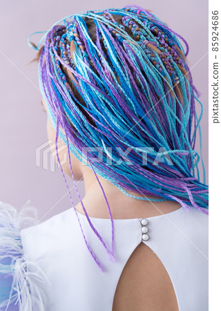 Rear view. Beautiful girl in an evening dress. Elegant dress with a neckline. The sleeves are decorated with feathers. Elegant big bow. Long multi-colored braids. Young beauty 85924686