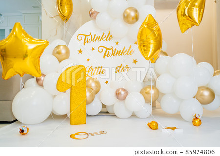 A photo zone for the first birthday of white and gold balloons and a figure one  85924806
