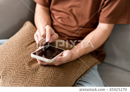Technology Concept The man sitting next to a pot of plant, putting a small pillow on his lap, and checking something on his smartphone 85925270