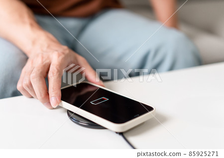 Technology Concept A person with his light blue jeans sitting on the couch and trying to charge his smartphone on the wireless battery charger Technology Concept A person with his light blue jeans sitting on the couch and trying to charge his smartphone on the wireless battery charger 85925271