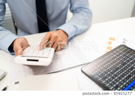 Working Man Conept The male officer sitting at his desk, holding the calculator, and pressing it Working Man Conept The male officer sitting at his desk, holding the calculator, and pressing it 85925277