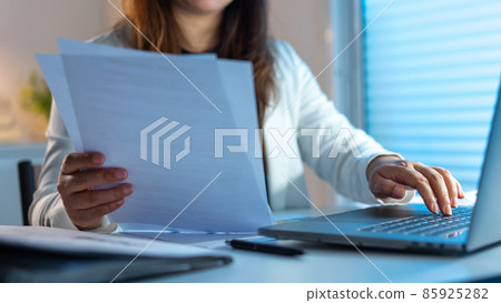 Overwork Concept The woman doing her work at late night by reading papers and typing them on the notebook Overwork Concept The woman doing her work at late night by reading papers and typing them on the notebook 85925282