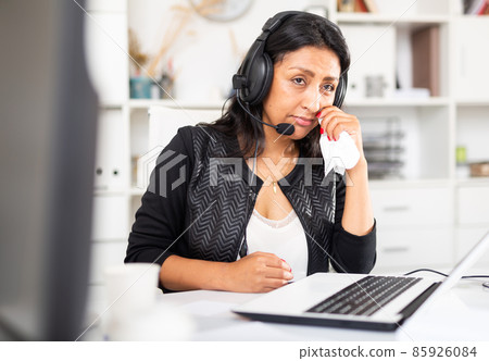 Upset woman wearing microphone headset at workplace in office Upset woman wearing microphone headset at workplace in office 85926084