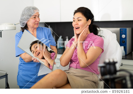Portrait of a satisfied young female patient after the procedure, looking in the mirror 85926181