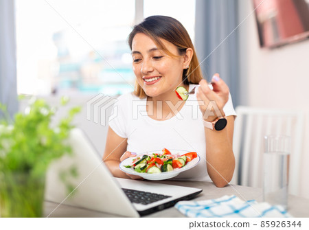 Housewife watching movie on laptop and eating vegetable salad 85926344