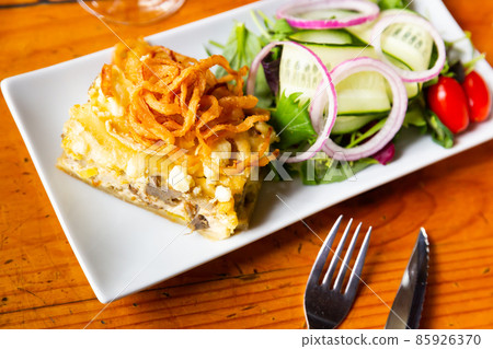 Slice of quiche Lorraine with fried onion rings and salad 85926370