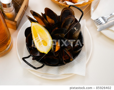 Steamed mussels with lemon wedge in metal serving pan Steamed mussels with lemon wedge in metal serving pan 85926402