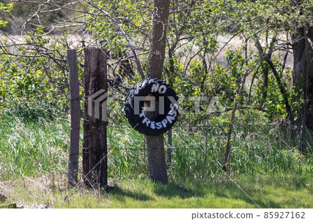 No Trespassing tire sign on barb wire fence  85927162