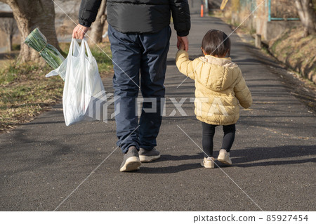Back view of a man walking with a child holding a shopping bag Back view of a man walking with a child holding a shopping bag 85927454