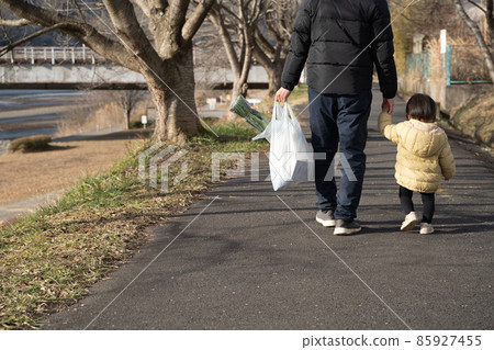 Back view of a man walking with a child holding a shopping bag Back view of a man walking with a child holding a shopping bag 85927455
