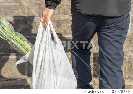 A man walking with a shopping bag down A man walking with a shopping bag down 85928280
