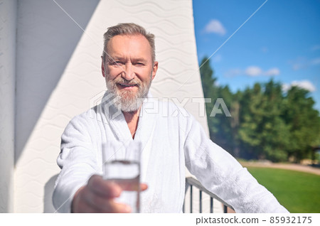 Friendly man offering a glass filled with liquid Friendly man offering a glass filled with liquid 85932175