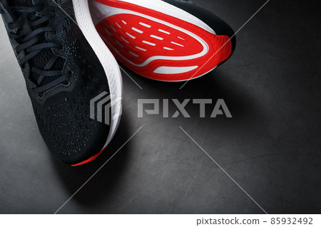 Black sports sneakers with red soles on a black background. 85932492