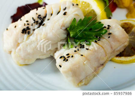 Cod prepared on steam, served at plate with greens and lemon 85937986