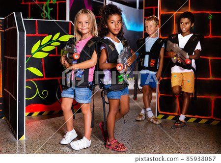 Smiling boy and girls aiming laser guns and playing laser tag game