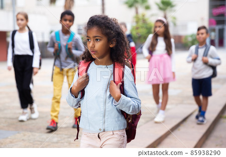 Positive schoolgirl standing near school, children on background Positive schoolgirl standing near school, children on background 85938290