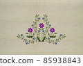 Embroidery of a bouquet with purple clementine flowers and delicate violets on a beige fabric background. 85938843