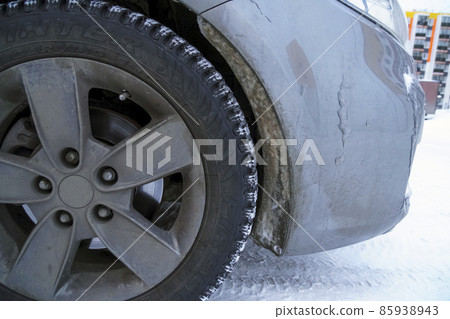 Front studded winter tire of car wheel arch covered with frozen snow in winter 85938943