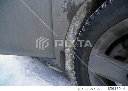 Studded winter tire of car wheel arch covered with frozen snow in winter 85938944