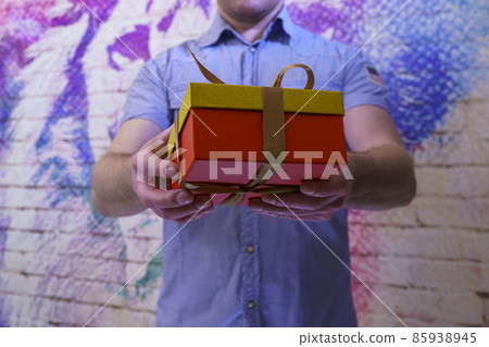 Man in blue shirt holds out a box with a gift indoors 85938945