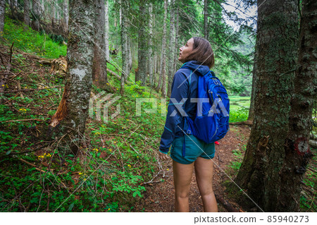 Young smiling woman with backpack walking on footpath in the forest Young smiling woman with backpack walking on footpath in the forest 85940273