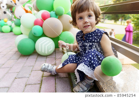 toddler girl with green balloons in dark blue dress 85945254