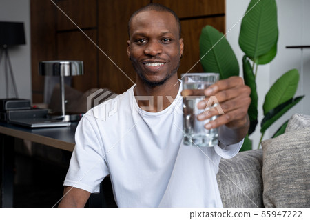 A handsome young black man holding a glass of fresh cool water in his hands A handsome young black man holding a glass of fresh cool water in his hands 85947222