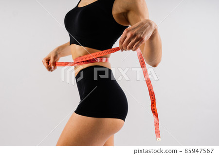 Fitness woman with tape measure showing her waist on studio background 85947567