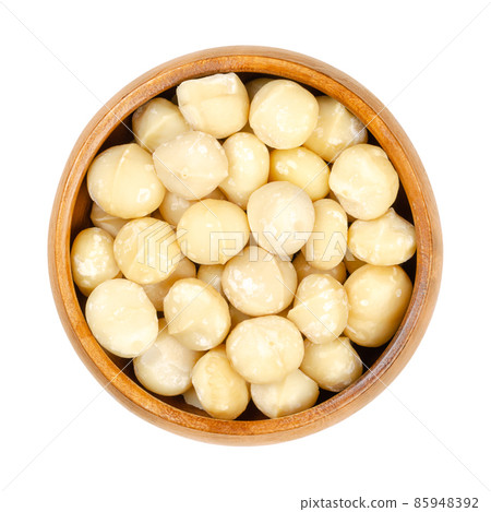 Shelled and dried macadamia nuts, in a wooden bowl. Also called Queensland, bush, maroochi, bauple or Hawaii nut. Wholesome snack. Close-up, from above, isolated on white background, macro food photo. 85948392