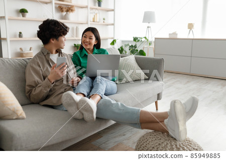 Asian couple using laptop and smartphone at home, cuddling on couch, watching videos, surfing internet, shopping online Asian couple using laptop and smartphone at home, cuddling on couch, watching videos, surfing internet, shopping online 85949885