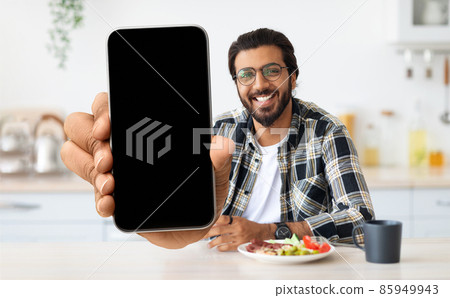 Handsome Indian Man Showing Blank Smartphone At Camera While Sitting In Kitchen 85949943