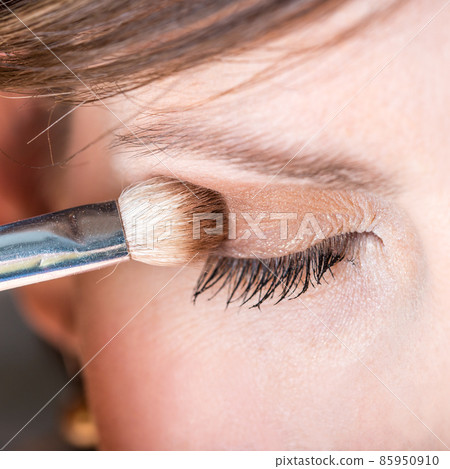 Woman applying eye shadow to her eyelid Woman applying eye shadow to her eyelid 85950910