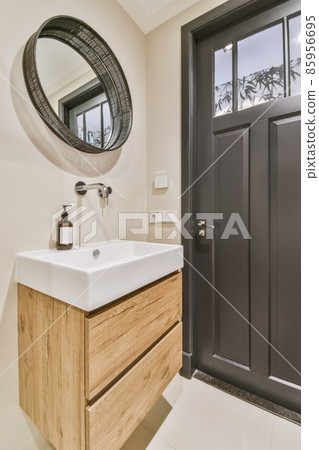 Bathroom corner with stylish sink and round mirror in black frame next to the door Bathroom corner with stylish sink and round mirror in black frame next to the door 85956695