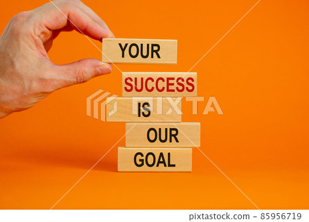 Wooden blocks with text 'your success is our goal'. Male hand. Beautiful orange background, copy space. Business concept. Wooden blocks with text 'your success is our goal'. Male hand. Beautiful orange background, copy space. Business concept. 85956719