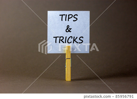 Tips and tricks symbol. White paper on wooden clothespin. Words 'Tips and tricks'. Beautiful grey background. Business and tips and tricks concept, copy space. Tips and tricks symbol. White paper on wooden clothespin. Words 'Tips and tricks'. Beautiful grey background. Business and tips and tricks concept, copy space. 85956791