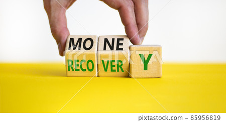 Money recovery symbol. Businessman turns wooden cubes and changes the word money to recovery. Beautiful yellow table, white background, copy space. Business and money recovery concept. 85956819