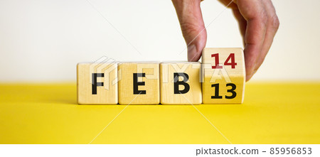 February 14 valentines day symbol. Hand turns the cube and changes the word 'Feb 13' to 'Feb 14'. Beautiful yellow table, white background, copy space. February 14 Valentines day concept. February 14 valentines day symbol. Hand turns the cube and changes the word 'Feb 13' to 'Feb 14'. Beautiful yellow table, white background, copy space. February 14 Valentines day concept. 85956853