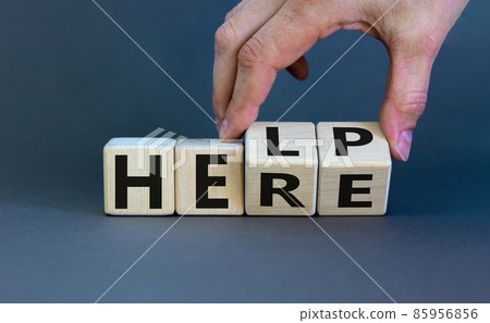 Help is here symbol. Businessman turns cubes and changes the word help to here. Beautiful grey background, copy space. Business, motivational and help is here concept. Help is here symbol. Businessman turns cubes and changes the word help to here. Beautiful grey background, copy space. Business, motivational and help is here concept. 85956856